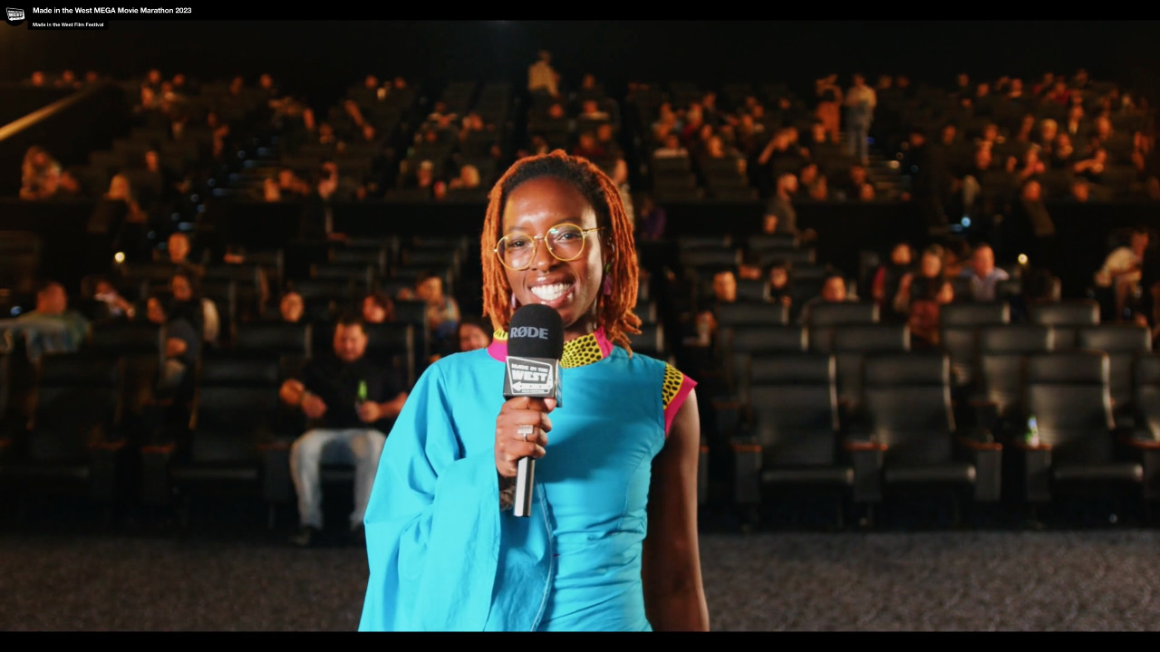 Woman in blue dress with microphone in front of a full cinema